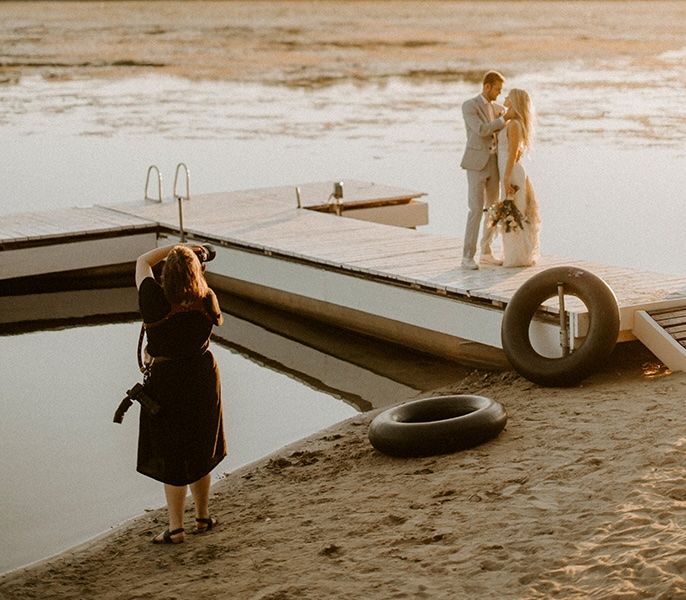 A photographer taking images of a couple on a dock during their wedding