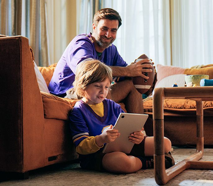 A father and son in their living room, the son looking at his tablet