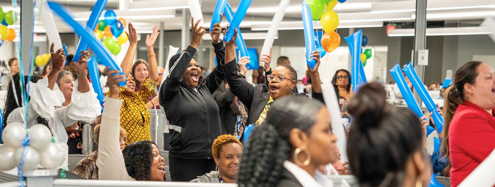 Spectrum employees celebrating during an an office event holding balloons over their heads