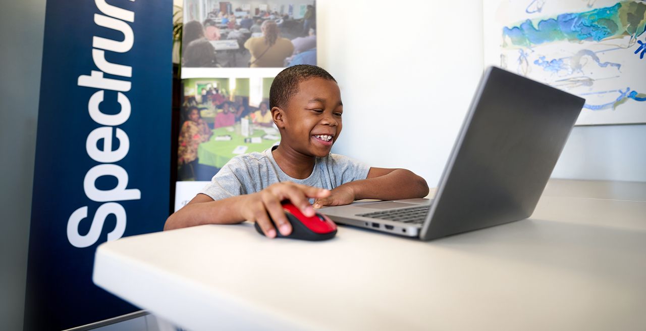 A student smiling as he uses a laptop 