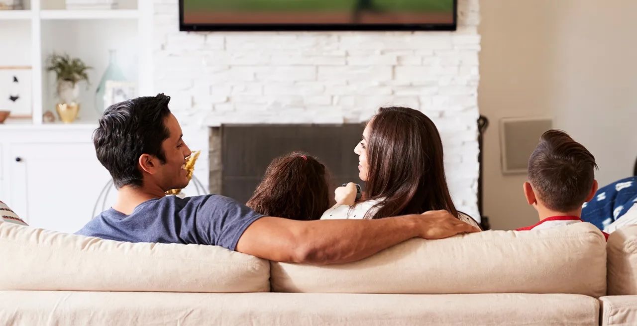 Family watching TV programming from their living room couch, viewed from behind