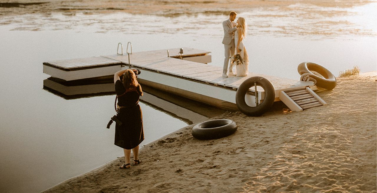 A photographer taking photos of a wedding couple posing on a dock