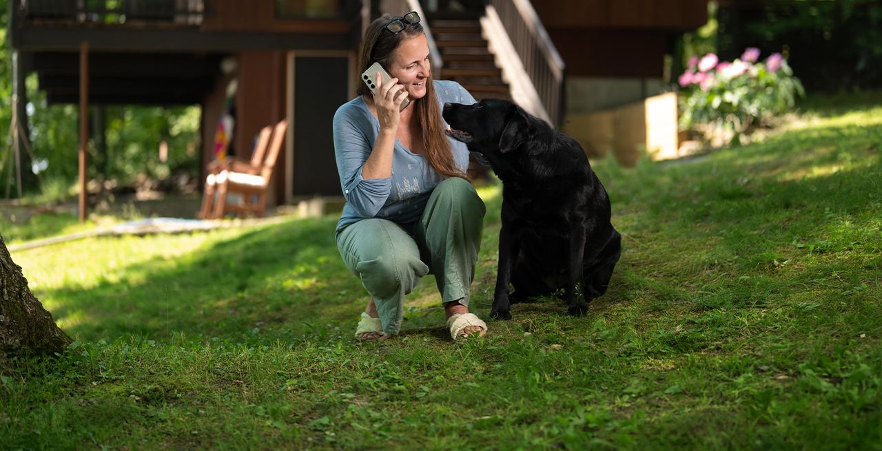 A woman using her smartphone in her yard with her dog