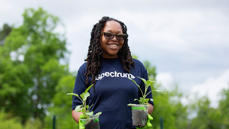 A Spectrum Community Impact volunteer holding two potted plants during an event