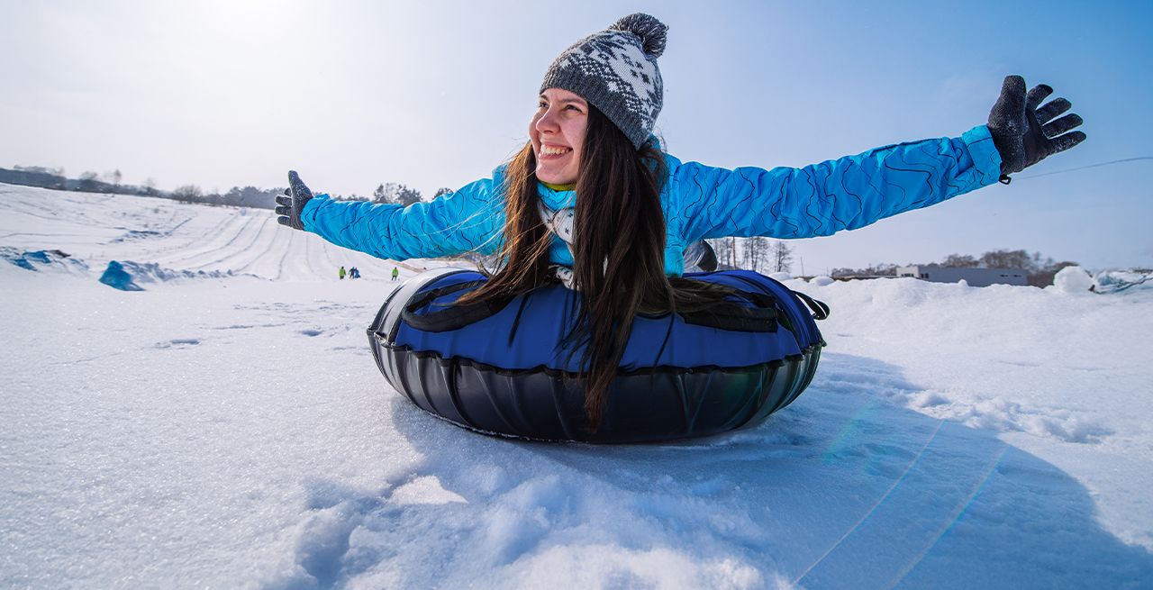 A woman sliding down a mountain on a snow tube, arms outstretched